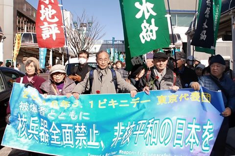 晴天の焼津市内を進む墓参行進東京代表団の先頭。「核兵器全面禁止、非核平和の日本を」と書かれた横断幕を横に並んだ5人が掲げている。
