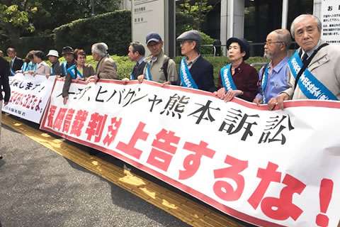 厚生労働省前の歩道で、「福岡高裁判決上告するな！」と書かれた横幕などを掲げて行動する被爆者たち。横幕は横に並んだ被爆者10人で持っているほど大きいもの。
