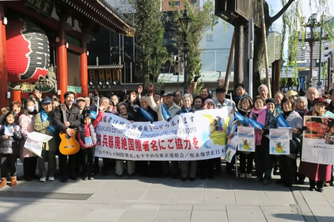 「核兵器廃絶国際署名にご協力を」と書かれた横断幕を中心に、街頭行動に参加した60人の笑顔の集合写真