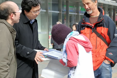 署名板にサインをする人と、そのとなりに立つ外国人と会話する行動参加者たち