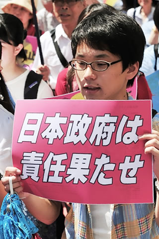 「日本政府は責任果たせ」と大きく書かれた紙を掲げてパレードに参加する若者。