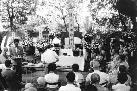 しつらえられた祭壇に花が供えられている。手前には椅子が並べられ、参列者が着席している。