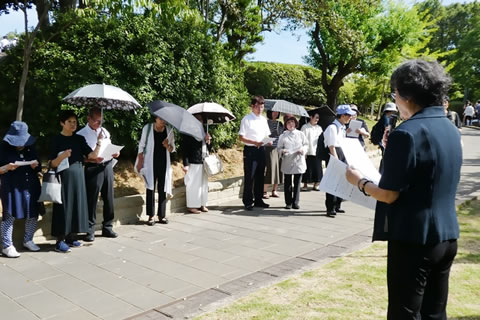 「東京の木」の前に立つ参加者たち。一人がマイクを持ちあいさつしている。