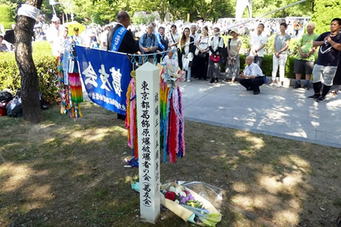 クスノキの前に集まった参加者。木の前には「葛友会」の旗や千羽鶴が提げられている。