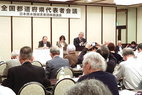 「全国都道府県代表者会議」と書かれた看板が掲げられた会場、参加者たちは着席し演台からの発言を聞いている