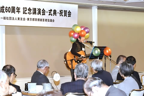 頭にさまざまな色の風船をいくつもつけてギターを弾き歌う人と、それを聞く参加者