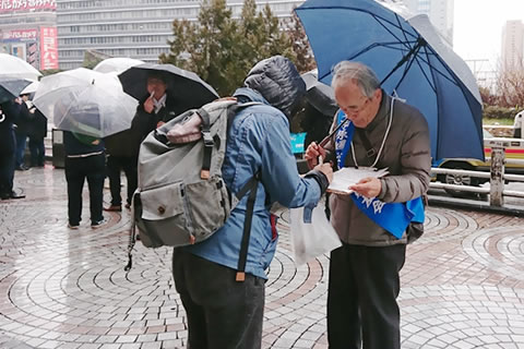 傘をさしながら署名板を持つ被爆者と、署名をする人