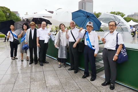 傘をさして平和公園内の川辺に立つ東友会代表たち。