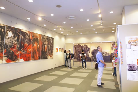 高さが人の身長ほど、幅も何メートルもある絵画が展示された会場で、展示物を見る人たち。