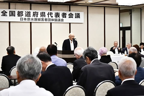 「全国都道府県代表者会議」と書かれた看板が掲げられた会場、参加者たちは着席し演台からの発言を聞いている