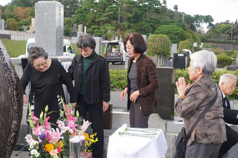 「原爆被害者の墓」の墓石の周囲で談笑する参加者、墓石に手を合わせる参加者