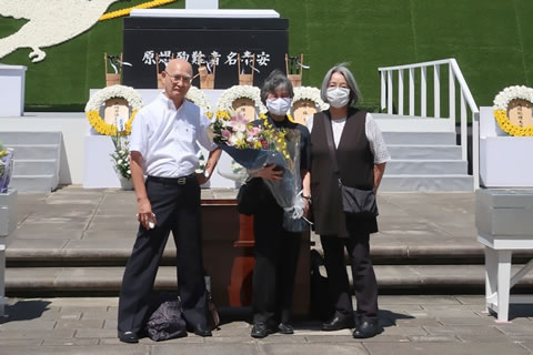 「原爆殉難者名奉安」と書かれた碑と献花台を背景に、花束を持つなどして立つ代表ら。