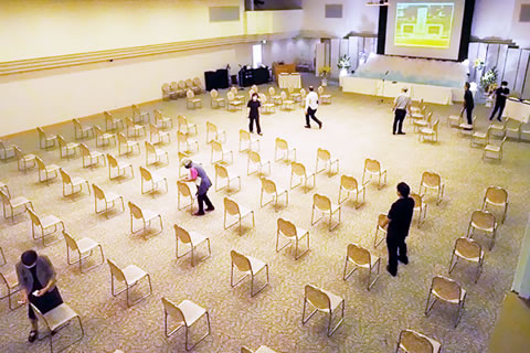 会場に間隔を置いて並べられた椅子と、準備をする人たち。
