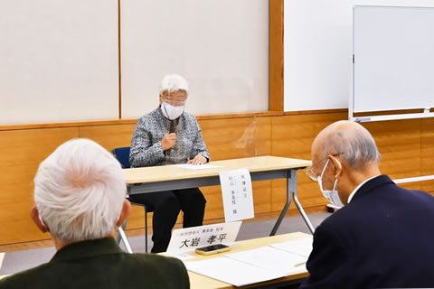 会場前方で参加者のほうを向いて着席し、マイクを使って話す村山さん。