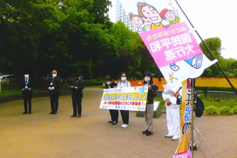 公園の広場のような場所で、マスクをし、間隔を開けて立つ数人の人たち。うち3名が、「核兵器禁止条約が発効しました 唯一の戦争被爆国の日本こそ参加を！」など書かれた横断幕を掲げている。「国民平和大行進」と書かれたのぼりも写っている。