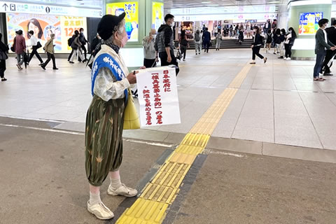 東友会のたすきを掛けた被爆者が広い地下通路に立ち、「日本政府に核兵器禁止条約の署名・批准を求める署名」と書かれた紙を取り付けた署名版を持って、通行人に呼びかけている。