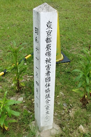 正面に「東京都原爆被害者団体協議会（東友会）」、側面に「昭和六十一年四月一日」と書かれた、四角柱の標柱。てっぺんは低い四角錐。
