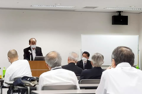 演台に立って話す澤原義明さん。並べられた長机に着席した参加者たちがそれを聴いている。