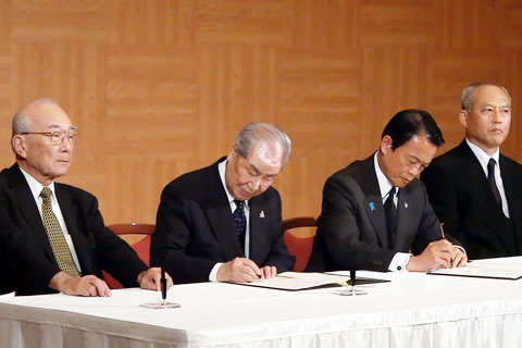 被団協代表2人と総理大臣、厚生労働大臣が一つのテーブルに横並びに座っている。被団協代表の1人と総理大臣がそれぞれ確認書に署名している場面。
