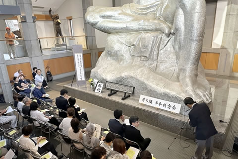 室内に置かれた平和祈念像の原形の前に椅子が並べられ、参加者が座っている。像の足元に、「井の頭 平和祈念会」ｔ横書きされた看板が置かれている。