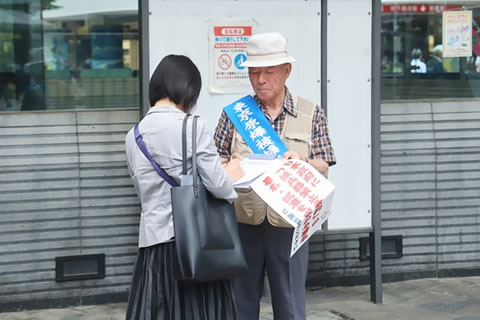 署名板を支え持つ東友会のタスキをかけた被爆者と、署名をする通行人。