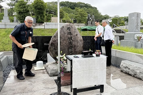 「原爆被害者の墓」の前には祭壇がしつらえられている。墓のそばに3人の人がおり、ひとりは白木の箱を持っている。