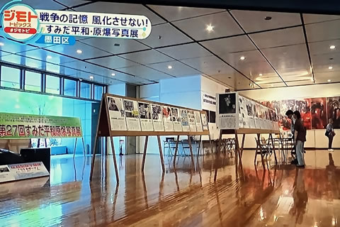 パネルが並べられた会場を写したテレビ映像の写真。「戦争の記憶 風化させない！ すみだ平和・げんばく写真展」の文字が左上に入っている。