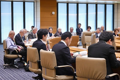 広い部屋に円形に並べられた曲線型の机に参加者たちが着席している。厚労省職員と思われる1人がマイクを使って話している。他の参加者たちは手元の資料に目を落としたり、発言者のほうを見たりしながら聴いている。