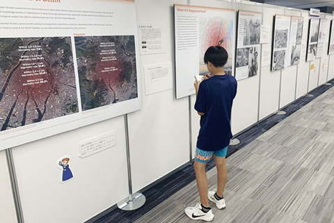 パネルの前に立ち、小さいメモ帳に何か書き込んでいる、小学生と思われる子ども。