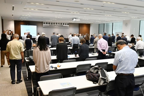 「全国都道府県代表者会議」と横書きされた看板が前方の天井から下げられた会場。参加者が、並べられた長机の席で立って黙とうしている。