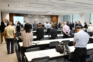 「全国都道府県代表者会議」と横書きされた看板が前方の天井から下げられた会場。参加者が、並べられた長机の席で立って黙とうしている。