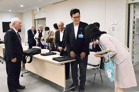 立ち上がり退出する身支度をする被爆者たちのひとりに、都議がひとり、頭を下げて挨拶をしている。挨拶を受ける被爆者が笑顔を向けて応じている。