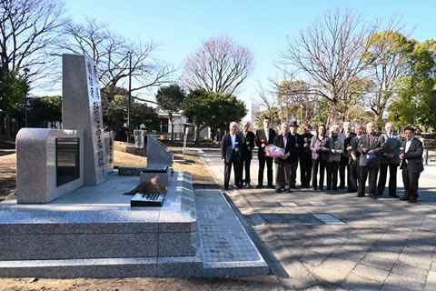 慰霊碑のわきに横一列に並ぶ役員。献花する花束を持っている役員もいる。
