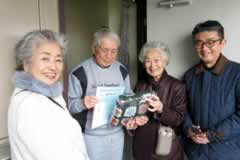 玄関ドアの前でカメラに向かってほほ笑む、訪問先の方と訪問者あわせて4名。