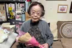 室内で、花束を持ってソファに座る訪問先の方。