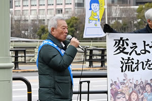 街頭に立ち、マイクを使って通行人に訴える、タスキを掛けた被爆者。