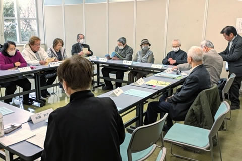 長方形に並べられた長机に、向き合う形で着席する参加者たち。机には紙の資料が配られている。