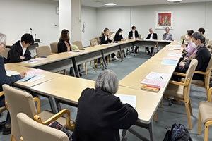 長方形に並べられた長机に、向き合う形で着席する参加者たち。机には紙の資料が配られている。