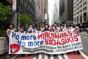 パレードに参加した要請代表団の先頭。9人が横並びになって横断幕を広げ持っている。横断幕には「No more HIROSHIMAS」「No more NAGASAKIS」と大きく横書きされ、折り鶴のイラストも配されている。「日本原水爆被害者団体協議会」「日本生活協同組合連合会」の2つの団体名も書かれている。