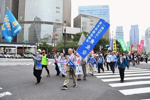被爆者2人が行進の先頭を歩いている。2人の一方は東友会ののぼり、一方は旗をを掲げていいる。その後ろに、被爆者数人が横断幕を広げ持って歩いており、そのあとにも被爆者たちが歩いている。被爆者はみな、東友会のタスキを掛けていう。被爆者たちのうしろに、団体名の書かれたのぼりを掲げるなどした参加者の列が続いている。
