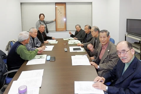 会議室で席に着く委員の面々。写っている9人のうち数人はカメラのほうを向いているが、向き合って話している様子の人たちもいる。。