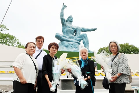 5名の東友会代表が、平和祈念像前に設置された献花台の前に花束をもって並んで立っている。