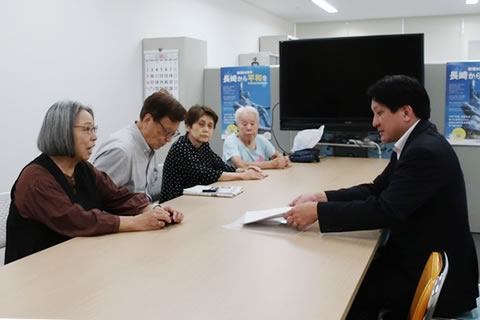 長机に向き合って座る長崎市職員1名と東友会代表4名。長崎市職員が書類を両手で受け取っている。