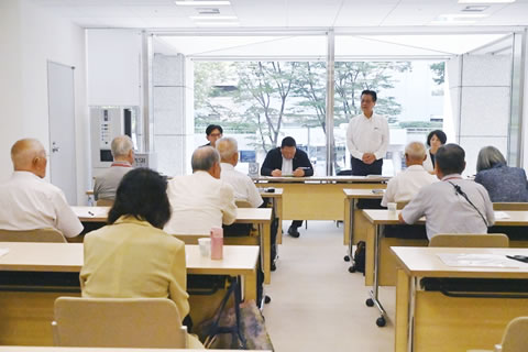 向かい合って並べられた机に座る議員らと東友会の参加者たち。議員団側4人のうち1人が立って発言しており、他の参加者たちは手元の資料に目を落としたり発言者のほうを見るなどしながら聞いている。