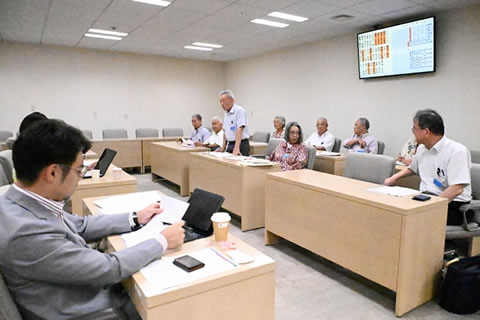 並べられた机に着席する東友会の代表たち。向かい合う形で並べられた机に議員らが着席しているが、写っているのは一人だけで、他はその1名の向こう側に隠れてしまっていて見えない。東友会側の1人が立って発言しており、他の参加者はそれを聞いている。