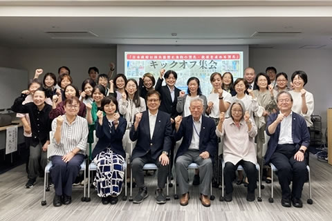 室内、参加者の集合写真。全員、肩のあたりにこぶしを掲げている。大半の人がが片手だけだが、両手を上げている人もいる。