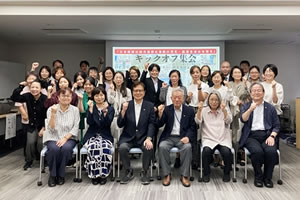 前方の壁に大型スクリーンが設置された広い部屋。スクリーンには原爆投下後間もないと思われる大きい建物内の写真と、「父、久吉は防空壕で生きていた」の文字が投影されている。スクリーン脇の演台で、中村さんが立ってマイクを使い話している。参加者は着席してスクリーンを見るなどしながら聞いている。